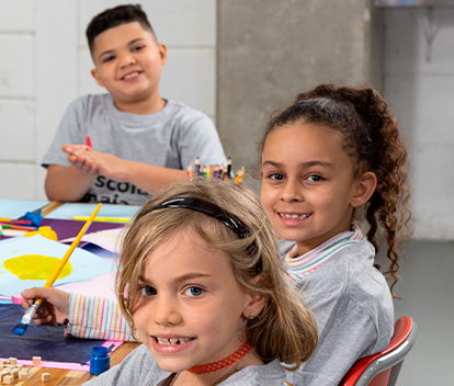 crianças sorrindo fazendo atividades escolares olhando para a câmera