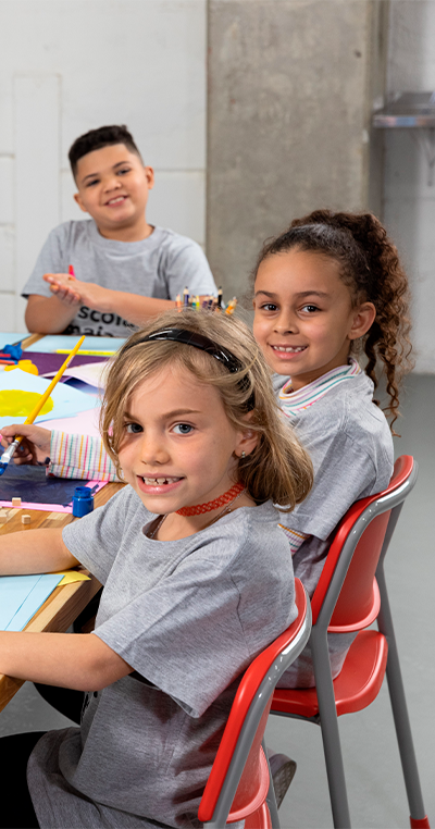 crianças sorrindo fazendo atividades escolares olhando para a câmera