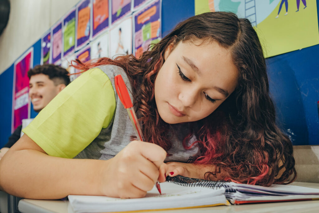 Garota estudante na sala de aula escrevendo em seu caderno com uma caneta vermelha