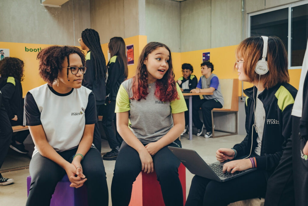 Três estudantes sentadas conversando na escola